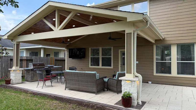 covered patio with wood ceiling gable roof outdoor kitchen and stone pillars in Houston TX