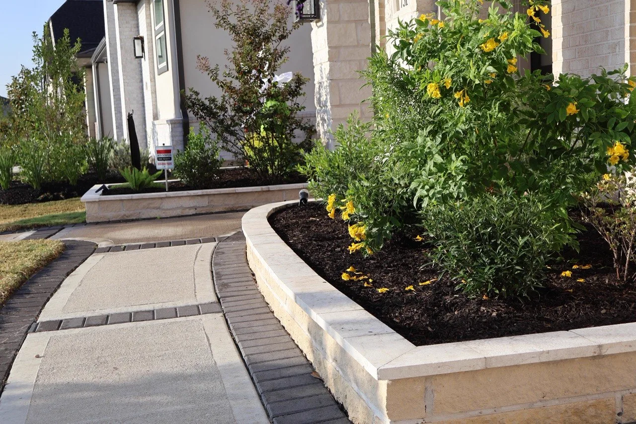Curved stone retaining wall planter with yellow flowers in Houston TX