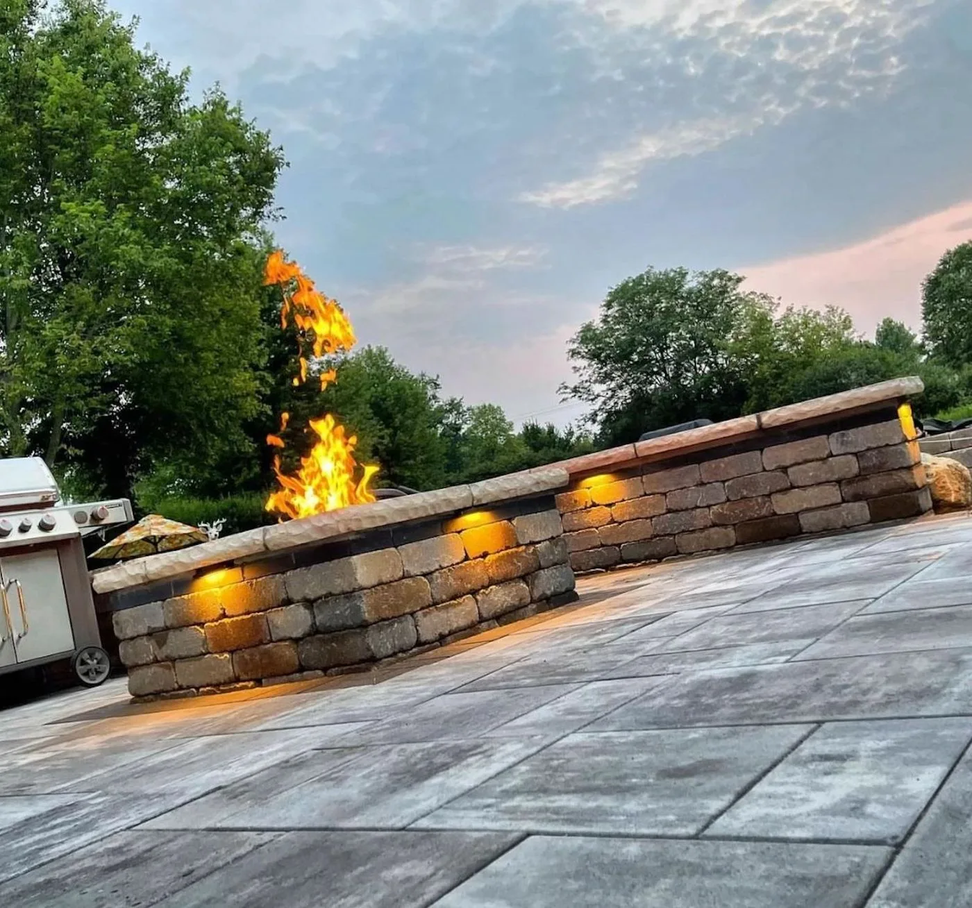 custom stone fire pit with seating wall and stamped concrete patio at dusk in Houston TX