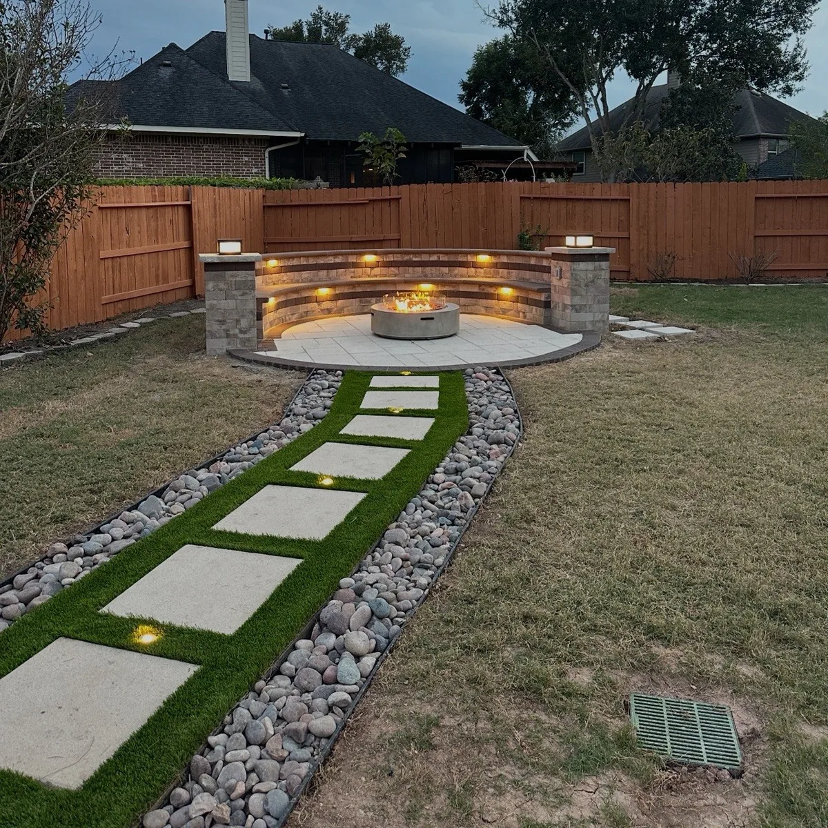 custom stone fire pit seating area with landscape lighting at dusk in Houston TX