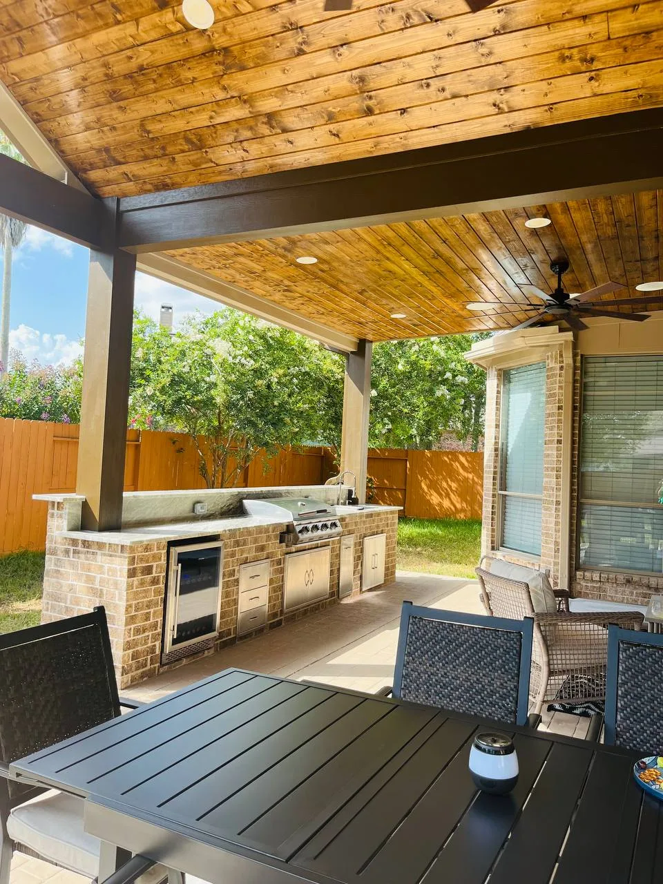 Outdoor kitchen with brick base, stainless grill, wine cooler under wood-ceiling covered patio in Houston TX