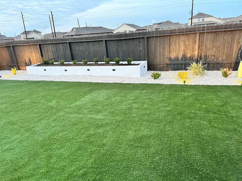 Artificial turf backyard with white raised planter bed and landscape lighting in Katy TX