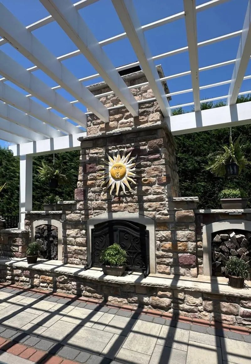Custom stone fireplace with ornate iron door under white pergola, paver patio in Katy TX