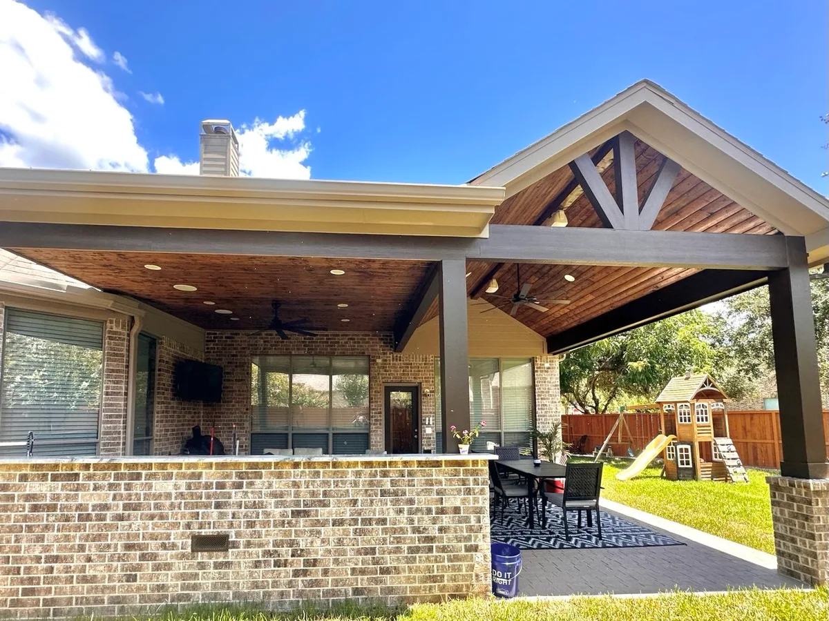 custom gable patio cover with fireplace TV ceiling fan and outdoor living at night in Houston TX