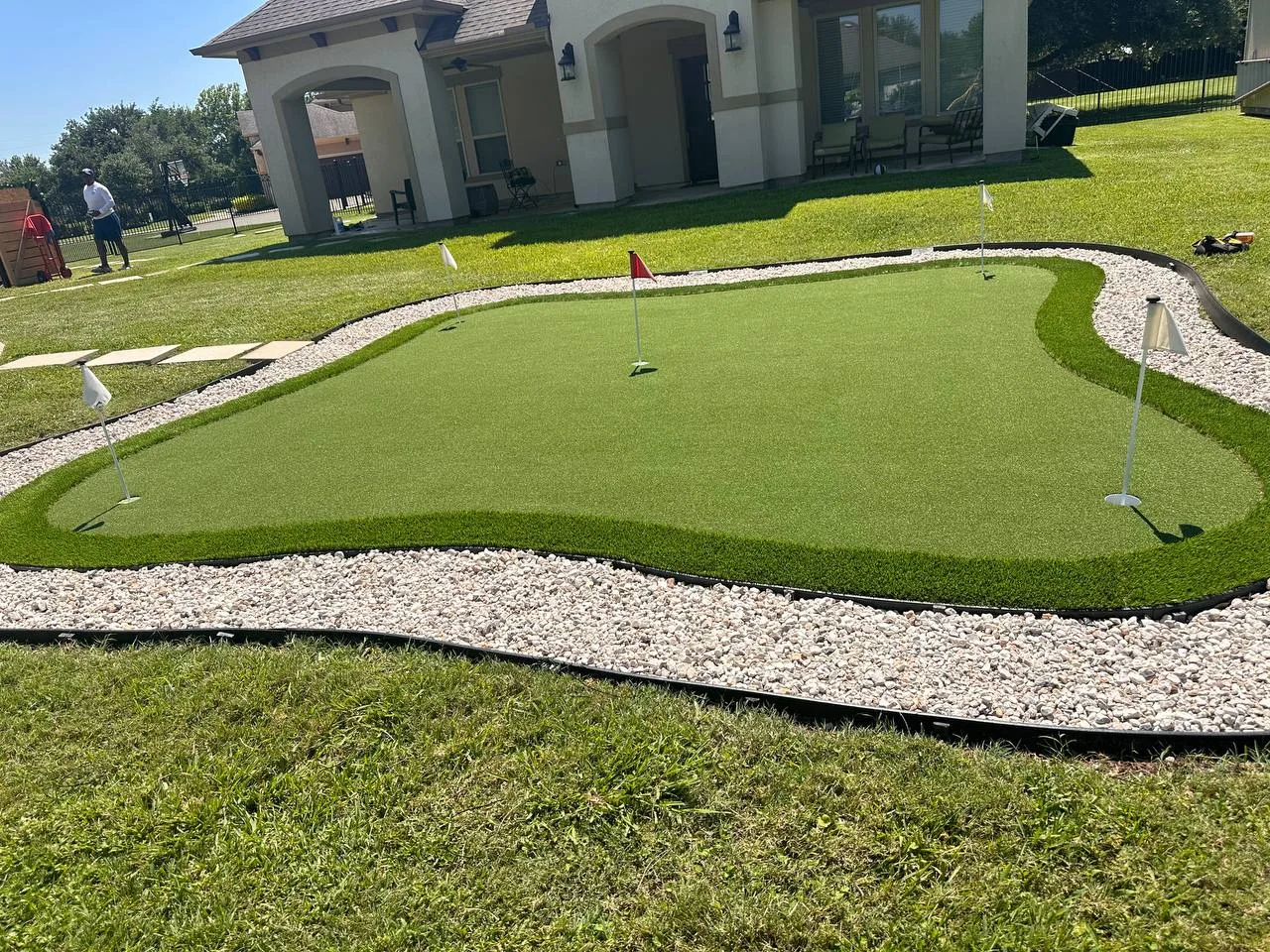 Custom artificial turf putting green with rock border and multiple holes in Pearland TX backyard