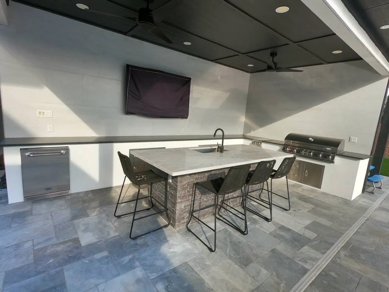 Modern outdoor kitchen with marble island, bar stools and outdoor TV in Pearland TX