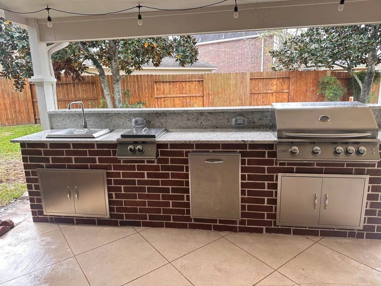 Outdoor kitchen with brick base, granite countertop, built-in grill and string lights in Pearland TX