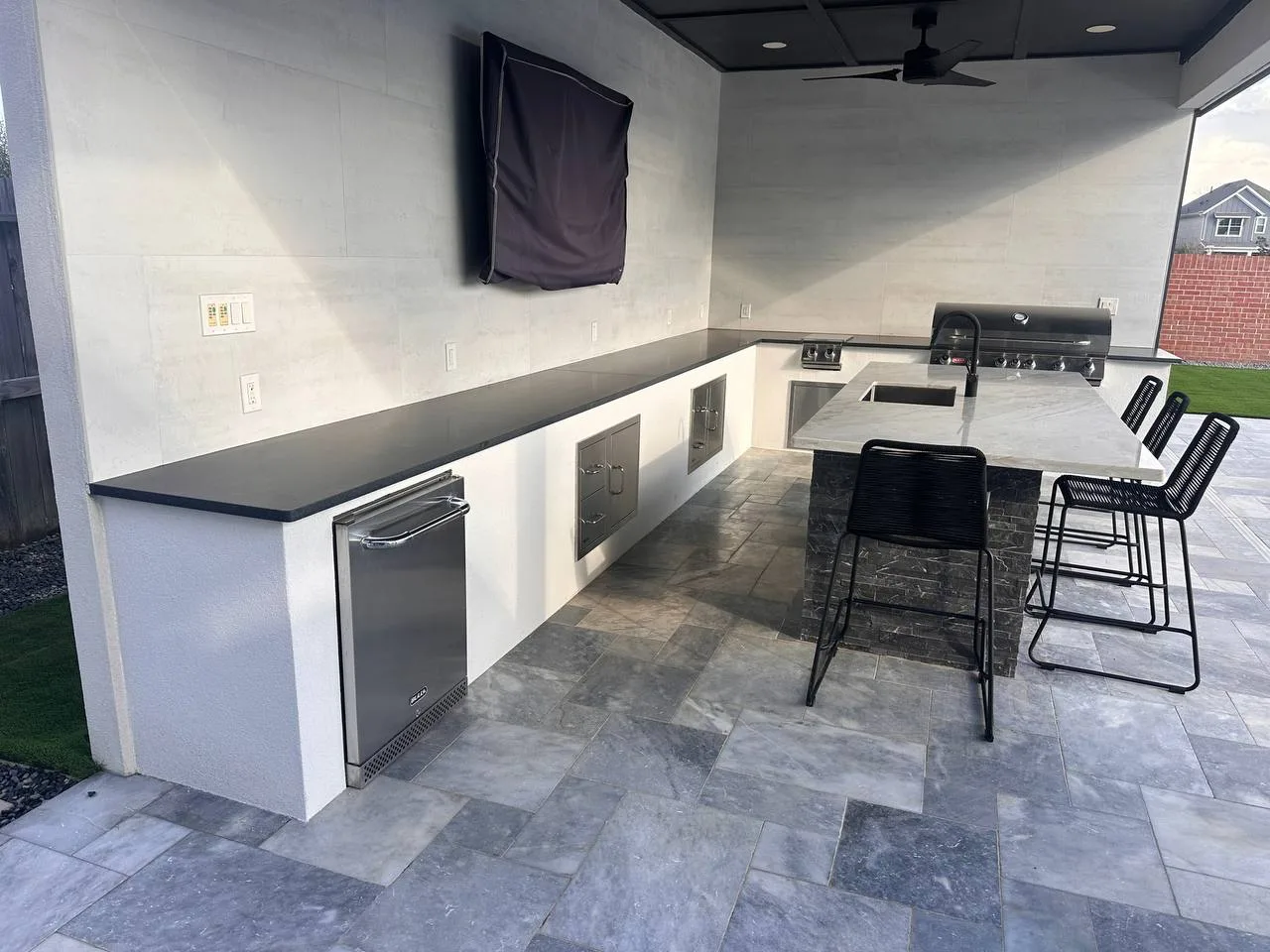 L-shaped outdoor kitchen with porcelain tile floor and stainless refrigerator in Pearland TX